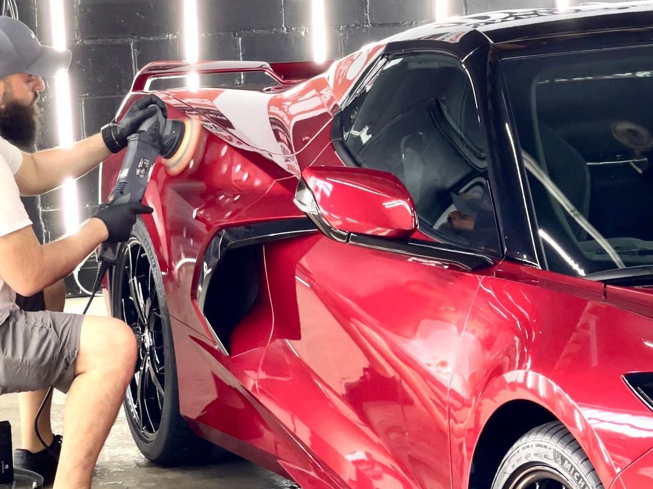 A man is polishing a red sports car in a garage.