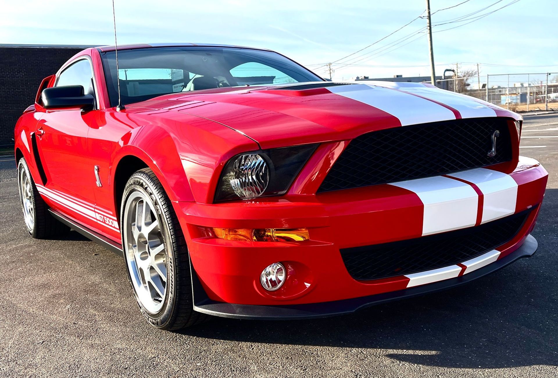 A red mustang with white stripes is parked on the side of the road.