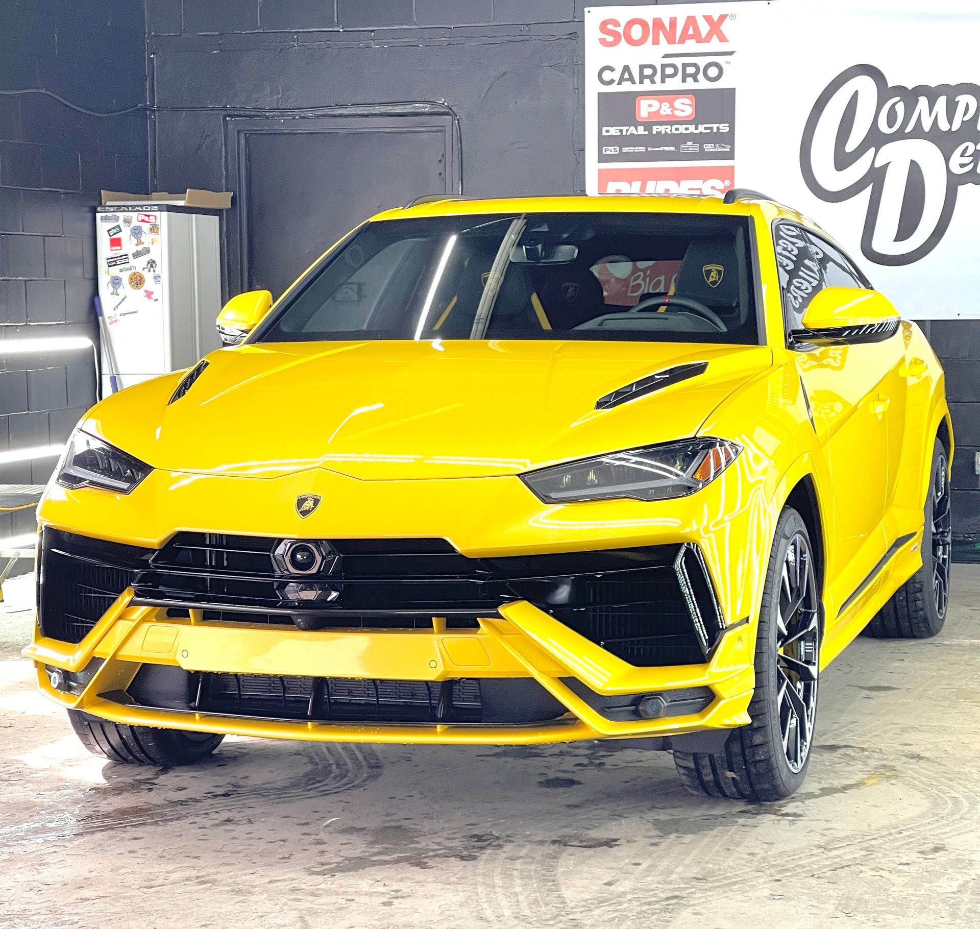 A yellow car is parked in front of a sonax carpro sign
