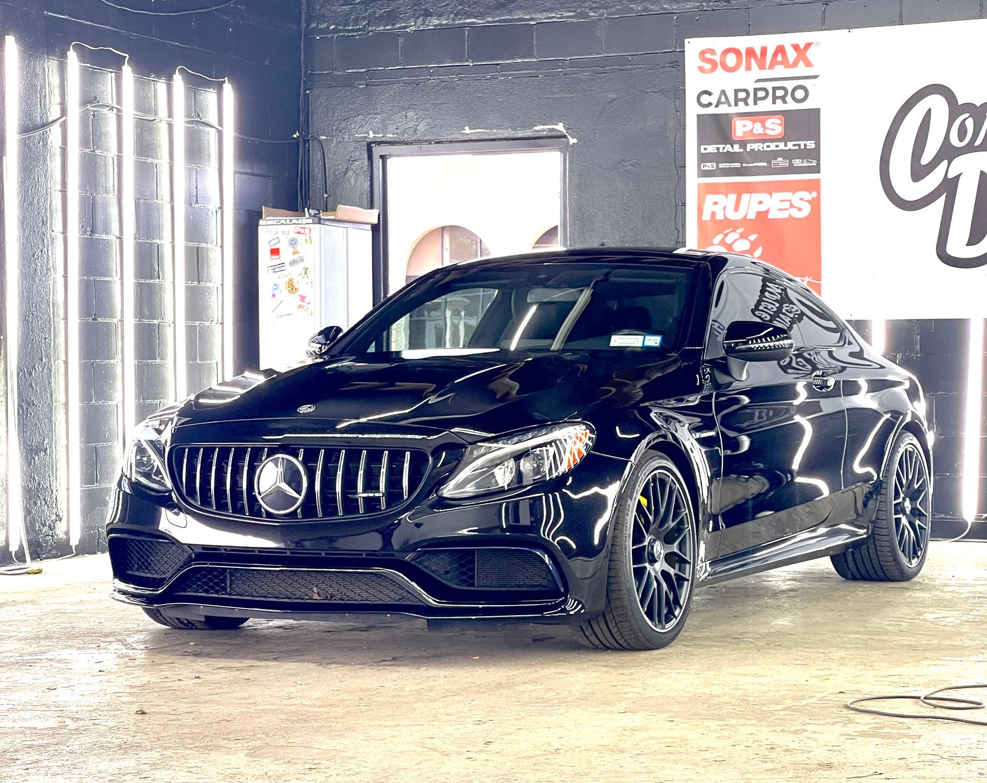 A black mercedes benz c63 amg coupe is parked in a garage.