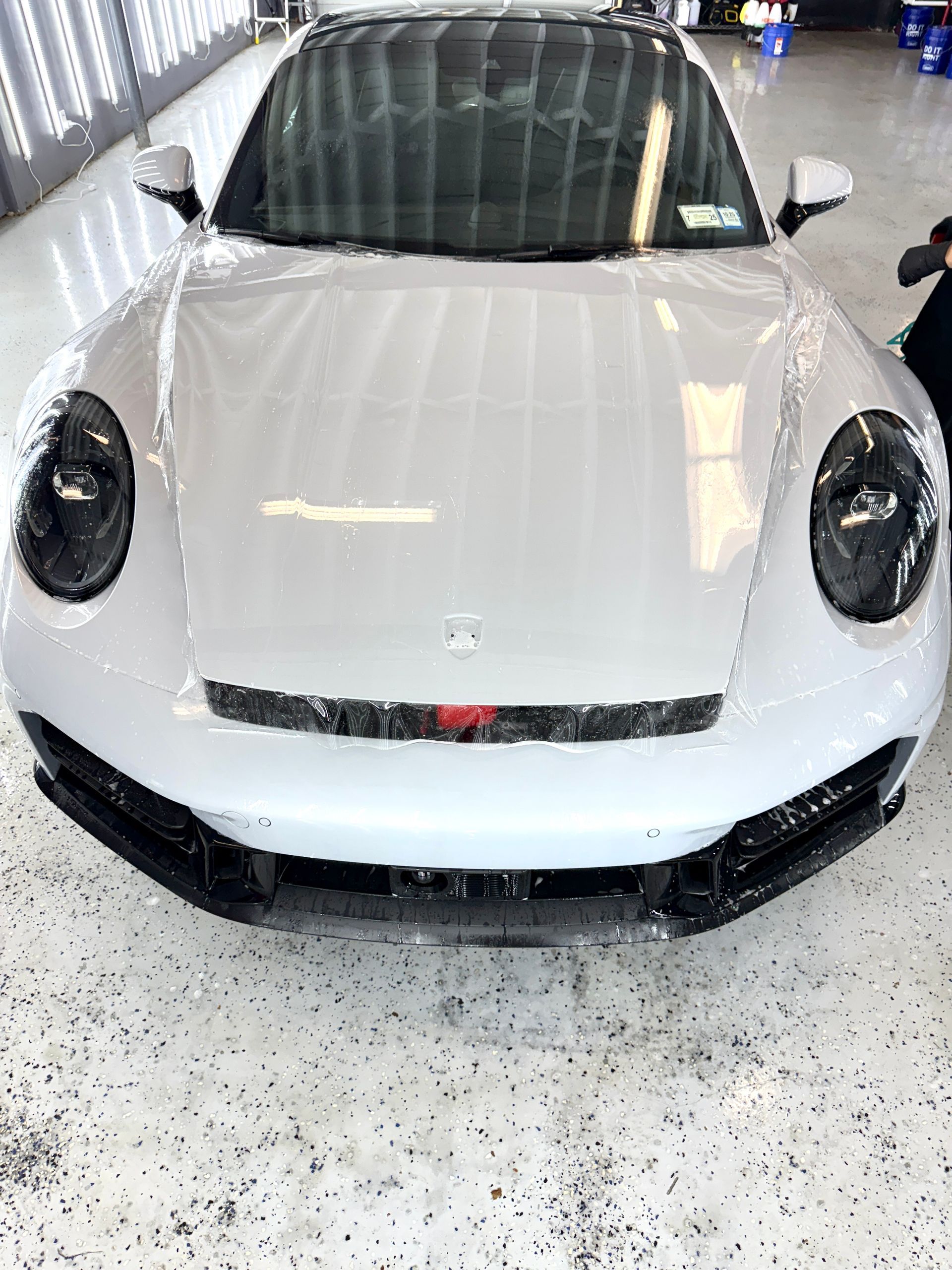 White sports car in a garage, front view with black accents and water droplets on the hood.