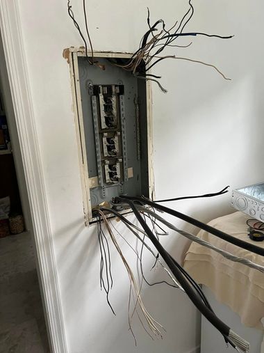 Open wall electrical panel with exposed wiring and cables extending out