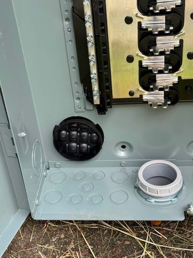 Open metal electrical panel with wiring, black vent cap, and white conduit fitting at the bottom.