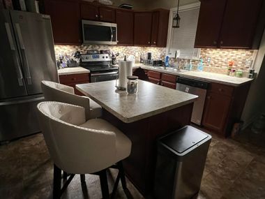Modern kitchen with dark cabinets, stainless appliances, a center island, and two cream barstools