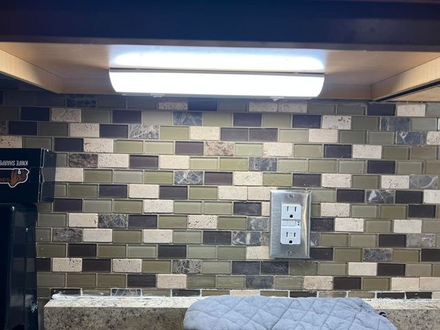 Kitchen backsplash with beige and gray tile, under-cabinet light, and a wall outlet.