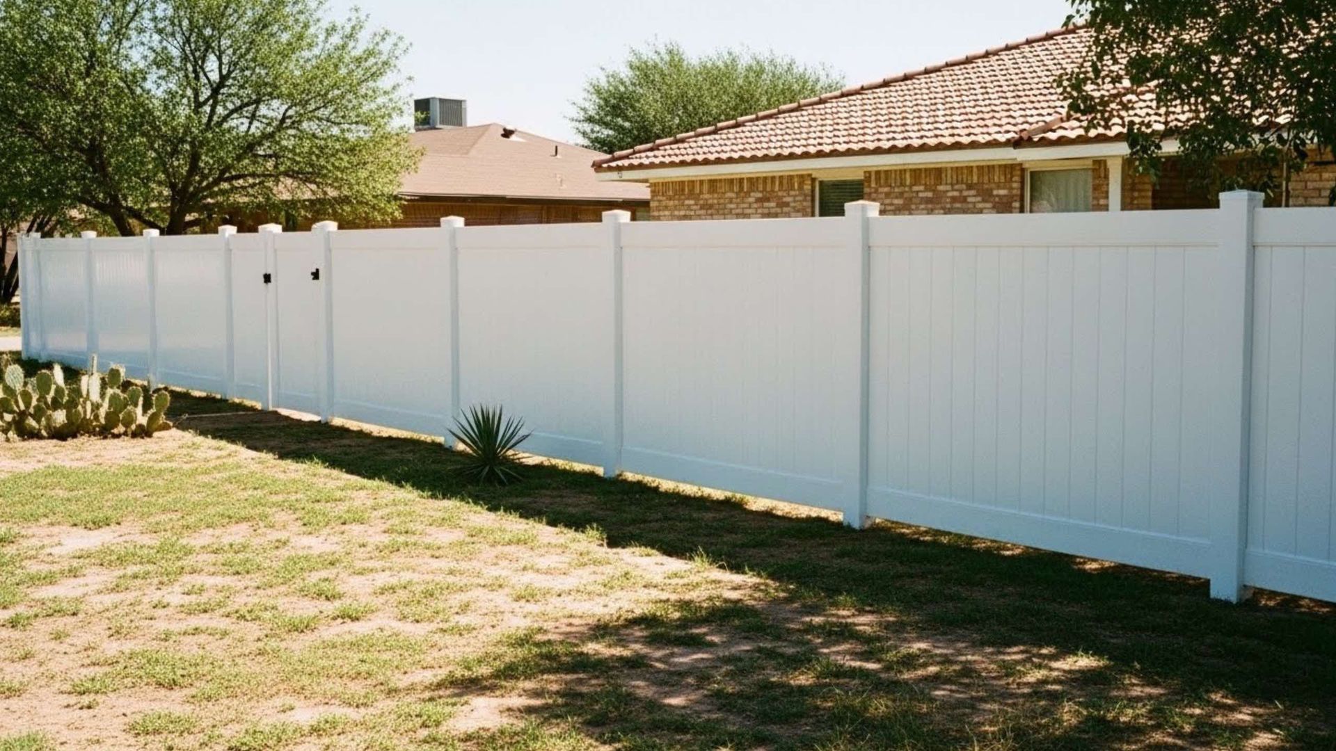 White vinyl privacy fence in a grassy yard, partially obscuring houses.