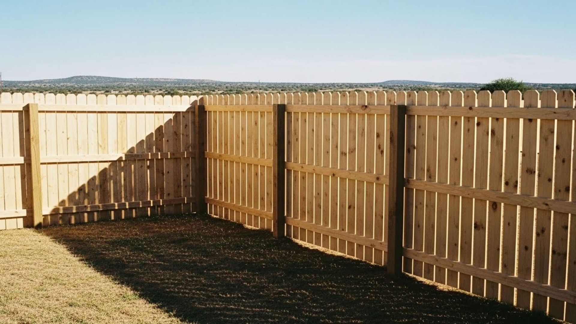 Wooden fence in a yard with a clear sky and distant trees.