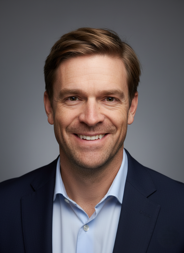 Studio headshot of Jared Stubbs in a navy blazer and light blue shirt against a gray background