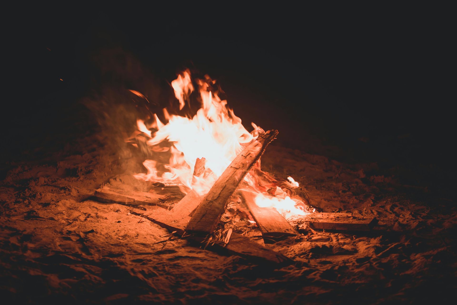 Campfire burning brightly at night, orange flames and embers.