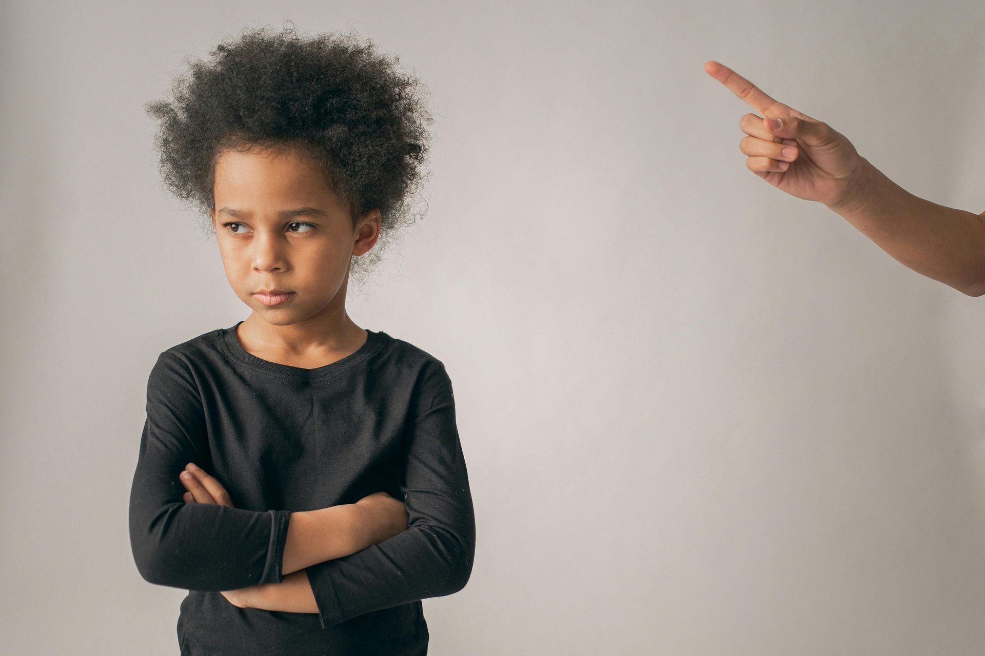 A person with their arms crossed and a serious expression stands while a finger points toward them from the side.
