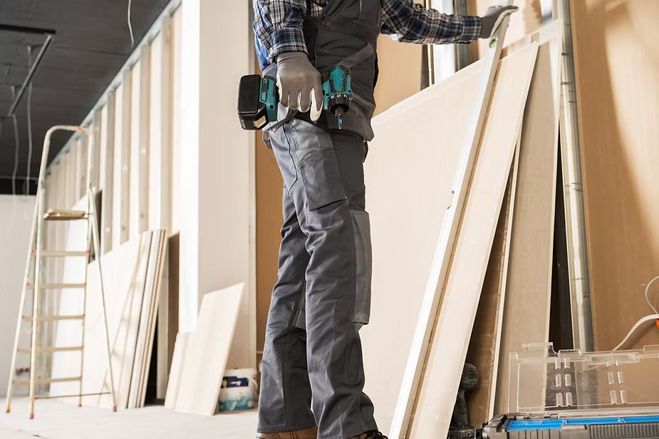 Worker installing wall panels at a construction site with stacked boards and a ladder nearby