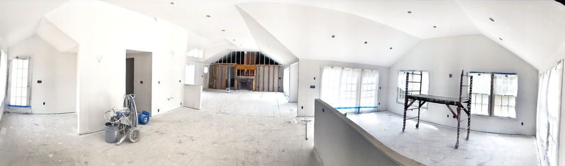 Bright unfinished attic room with white walls, exposed beams, windows, and construction materials scattered around.