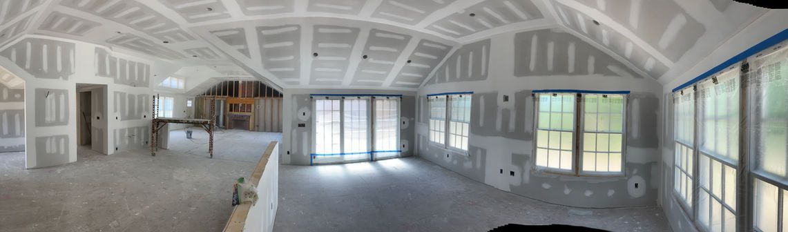 Panoramic view of an unfinished white interior room with exposed beams and large windows