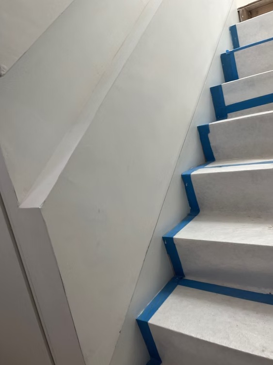 Staircase with white walls and steps edged in blue tape, viewed from below.