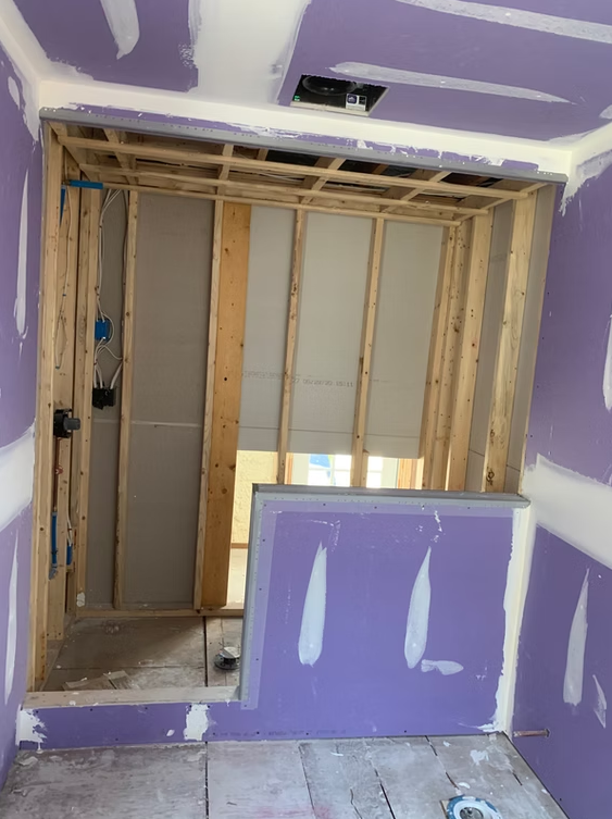 Partially demolished room with exposed studs, purple drywall, and debris on the floor