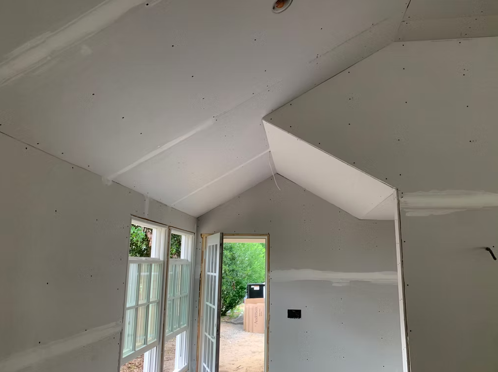 White plaster room with sloped ceiling, open door, and windows letting in daylight.