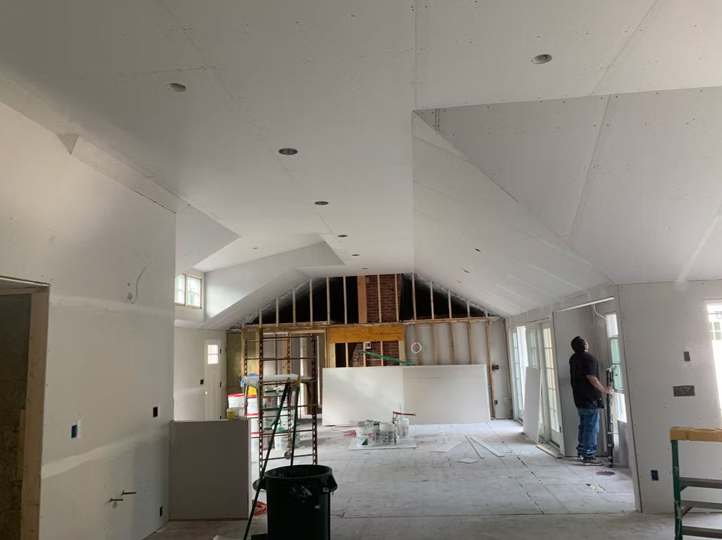 Interior of a room under renovation with exposed framing, tools, and a worker near the right wall.