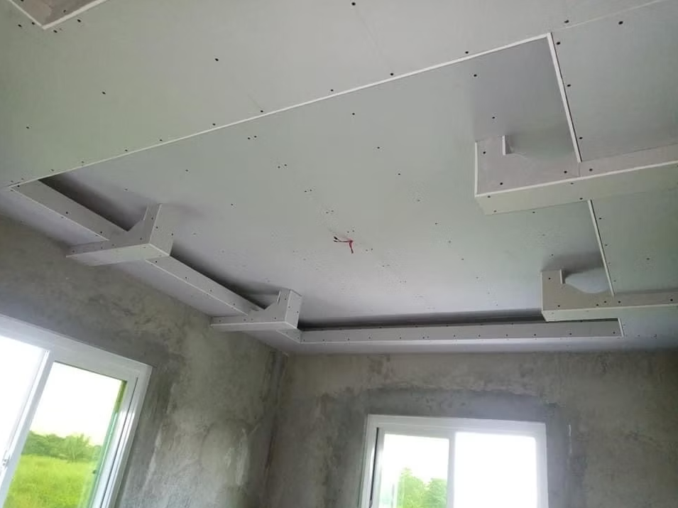 Unfinished room ceiling with drywall cutouts and recessed lighting openings above windows.