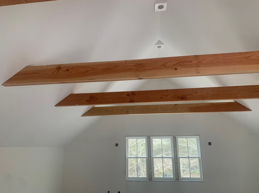 Wooden ceiling beams above a small window in a white room.