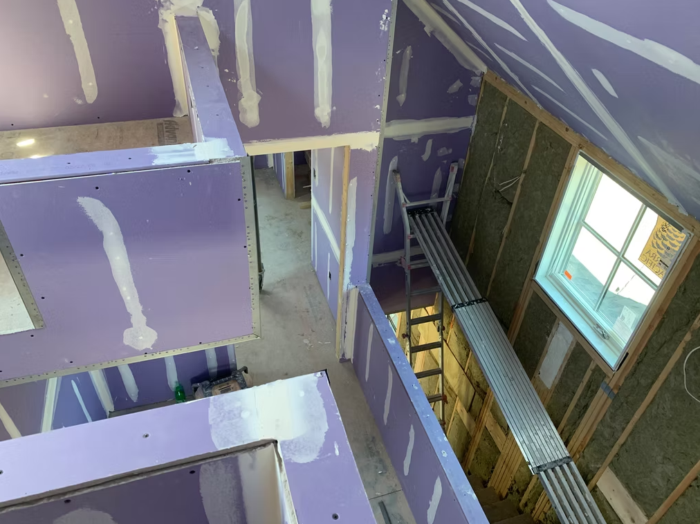 Interior of an unfinished building with purple drywall, exposed framing, and windows along a stairwell.
