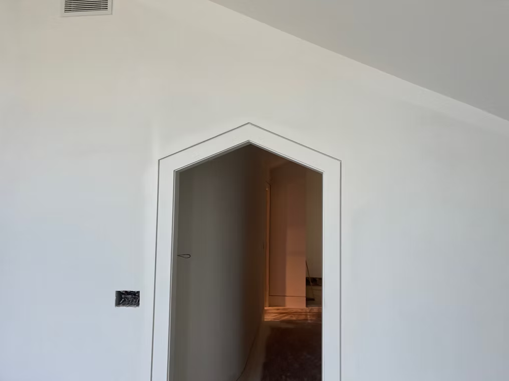 White wall with an octagonal doorway opening into a dim hallway or room