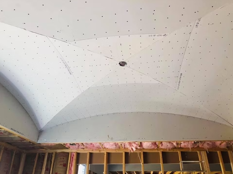 Curved white ceiling under construction with exposed wood framing and a small central fixture.