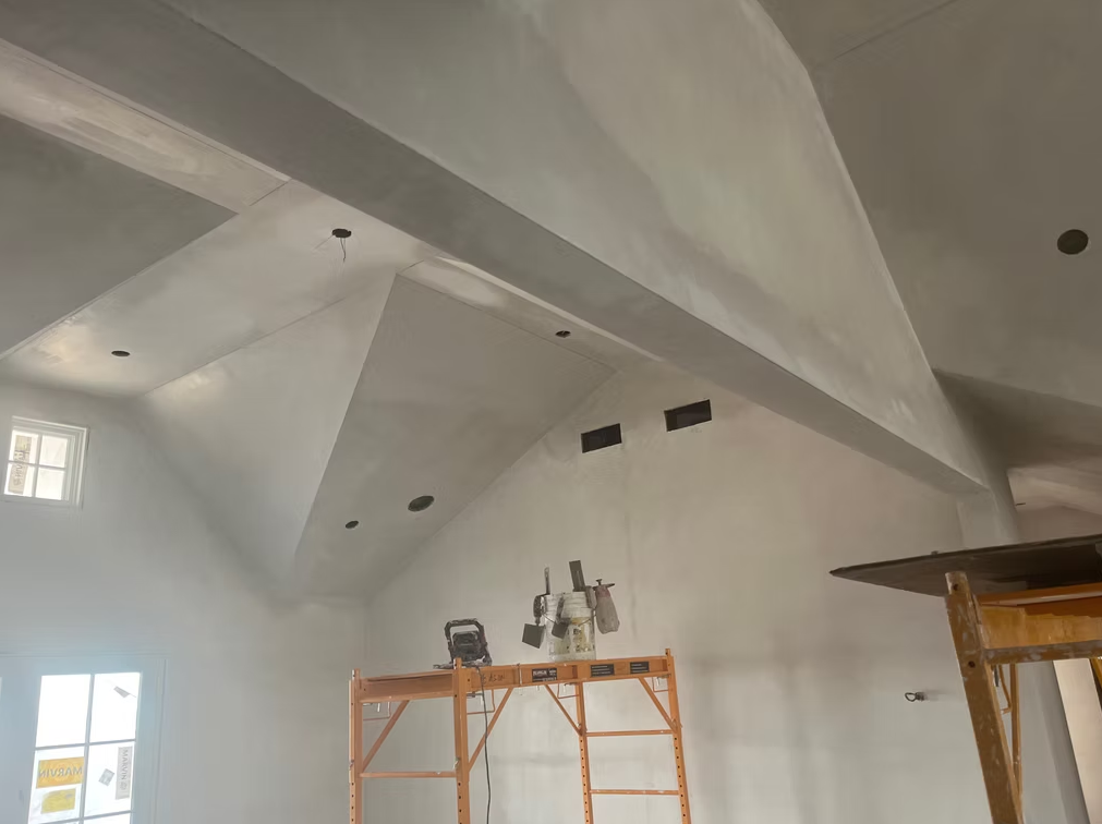 Indoor room with vaulted white ceiling, construction scaffolding, and a ladder near a window.