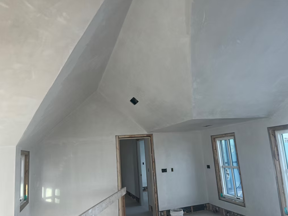 Empty white room with slanted ceiling, open doorway, and windows letting in daylight