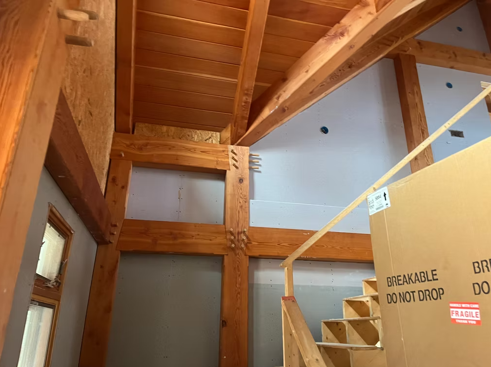 Wooden stairwell with exposed beams and a sign reading “ELEVATOR DO NOT DROP” on a wall panel.