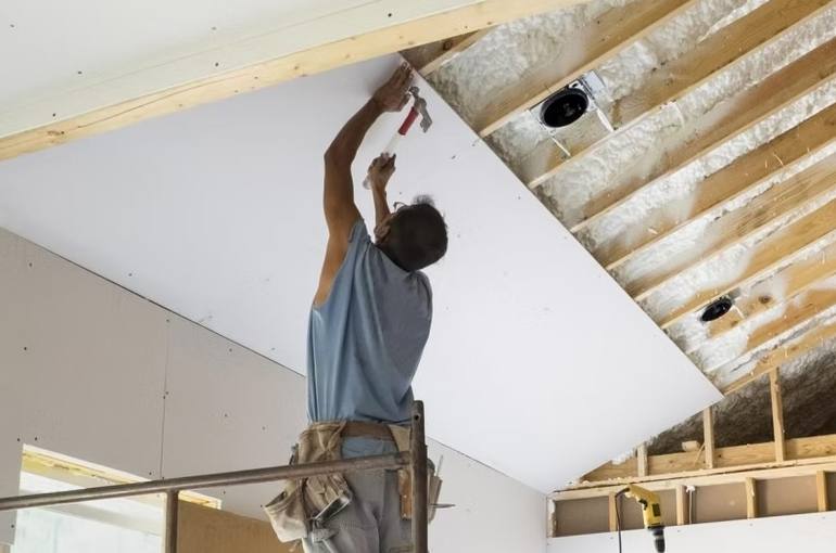 Worker installing drywall on a ceiling in an unfinished room
