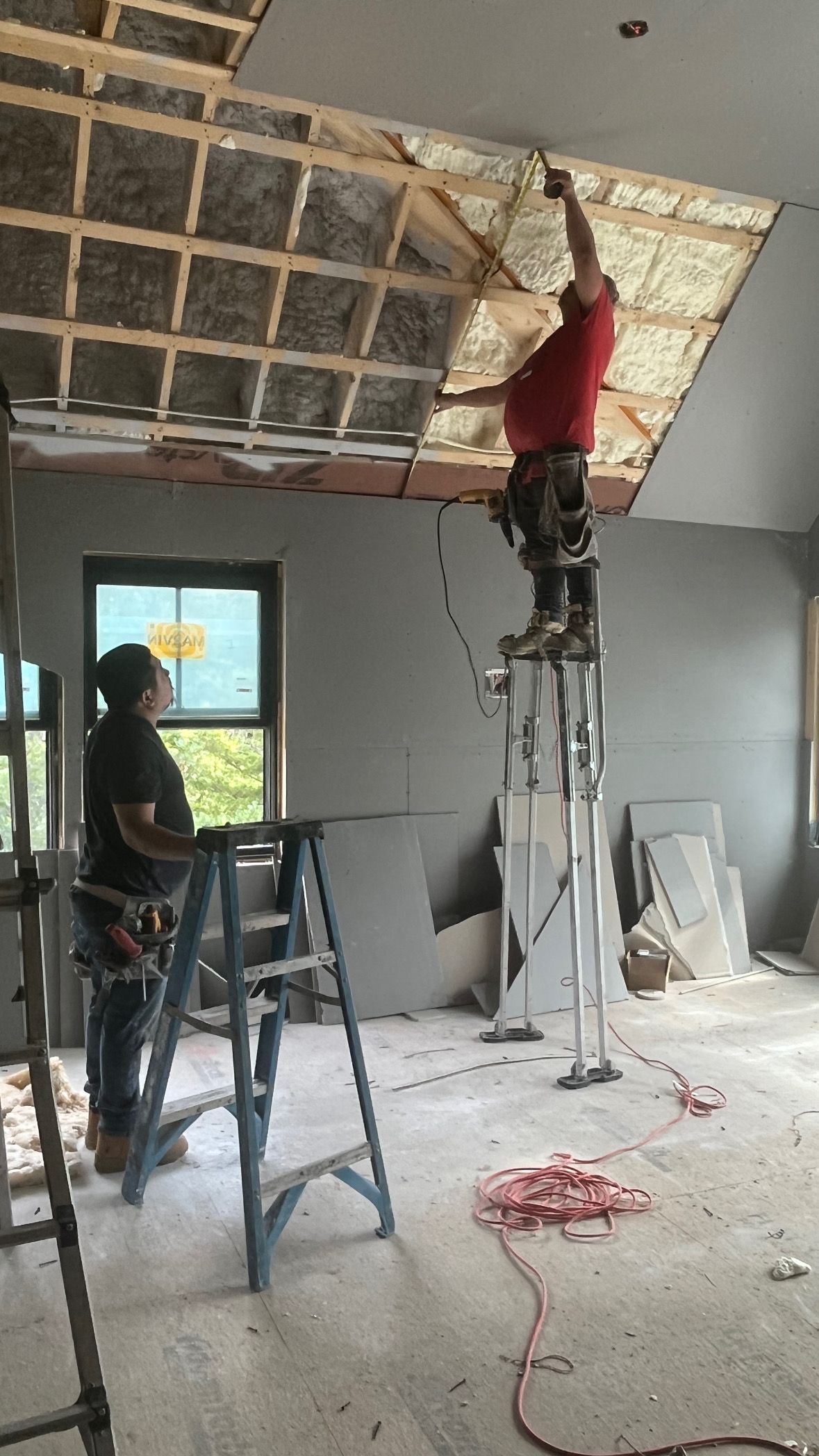 Workers repairing a damaged ceiling inside a room, one on a ladder removing panels, debris on the floor