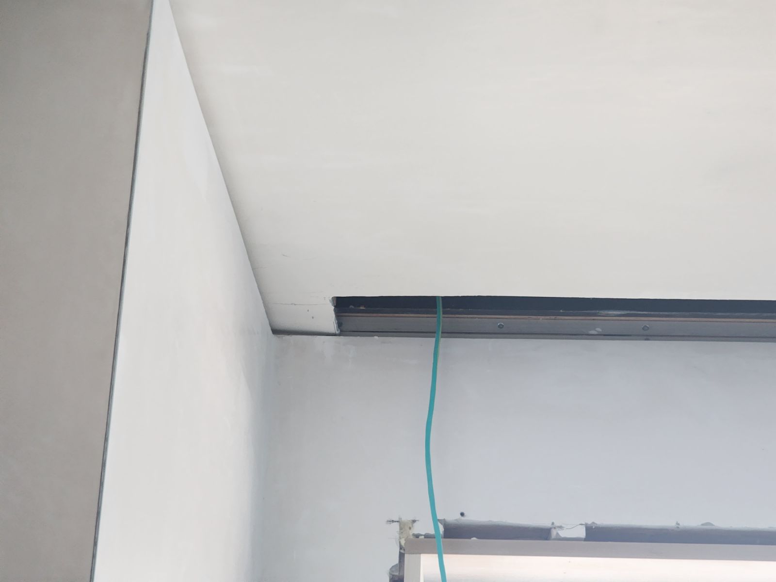 Partially installed ceiling with exposed black trim and a hanging green wire in a white room