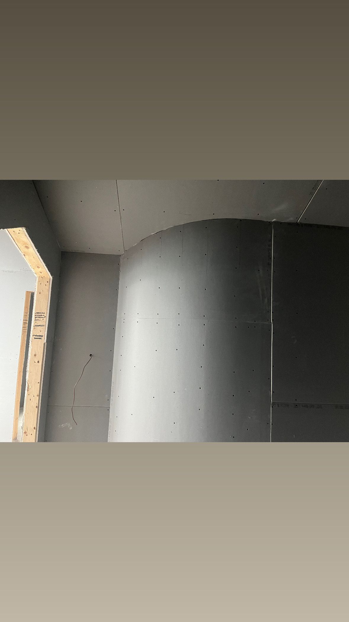 Close-up of a gray wall corner with a dark curved surface and a partially visible wooden beam on the left