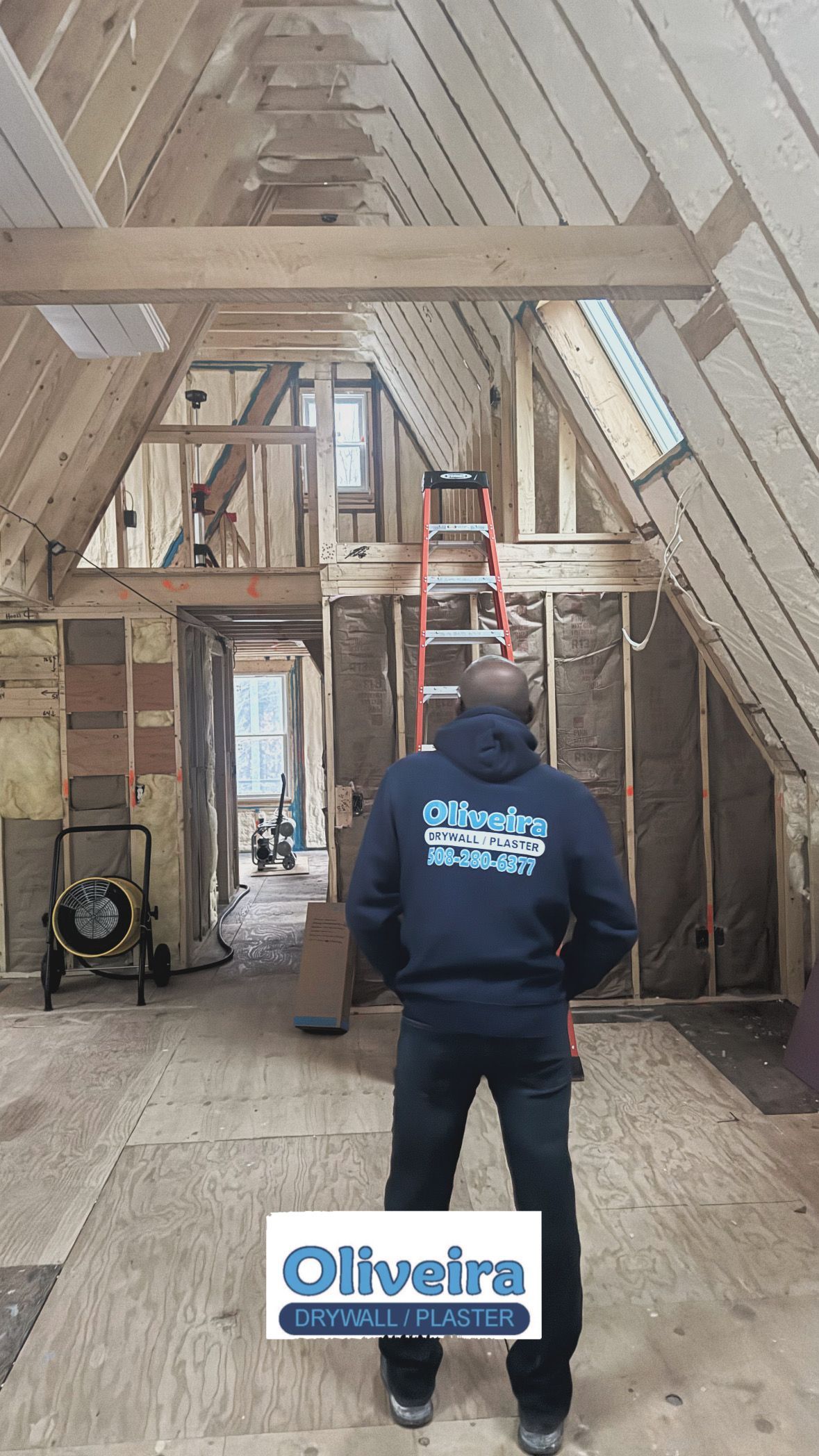 Person standing in a partially renovated attic with exposed beams and a ladder in the center.