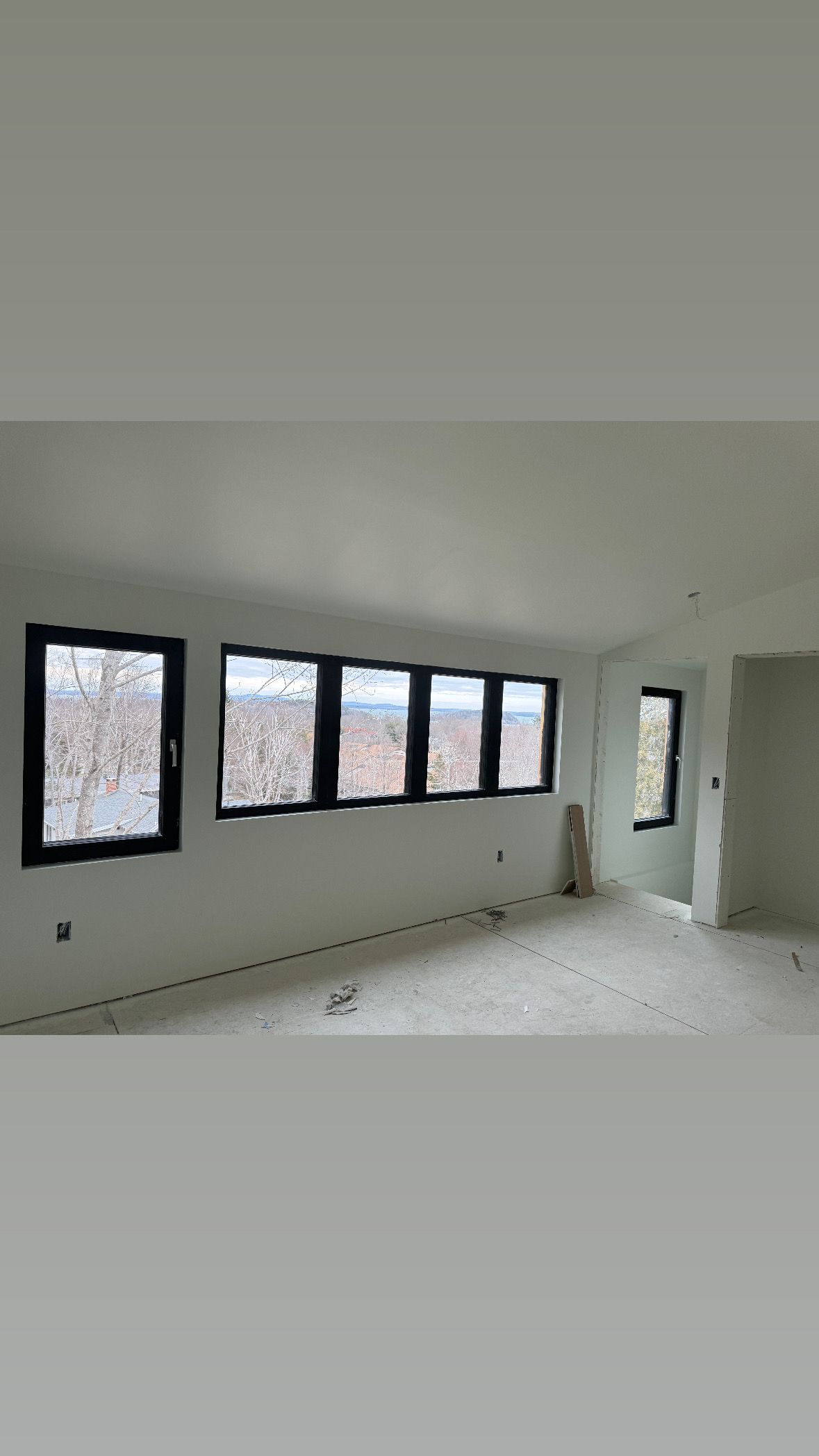 Bright empty room with white walls, black-framed windows, and a tiled floor during renovation