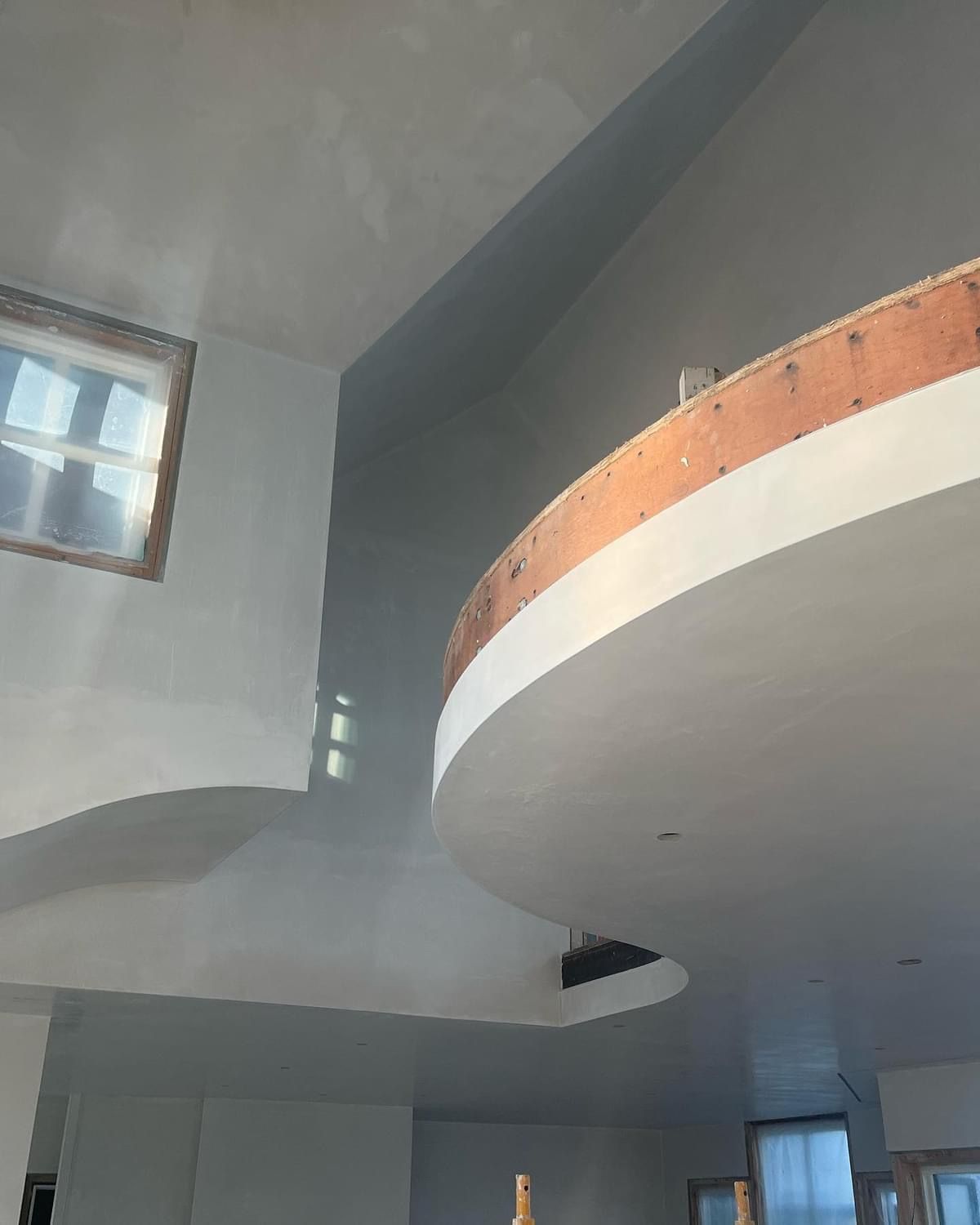 Modern interior with curved white balconies, wood railing, and high windows under a slanted ceiling