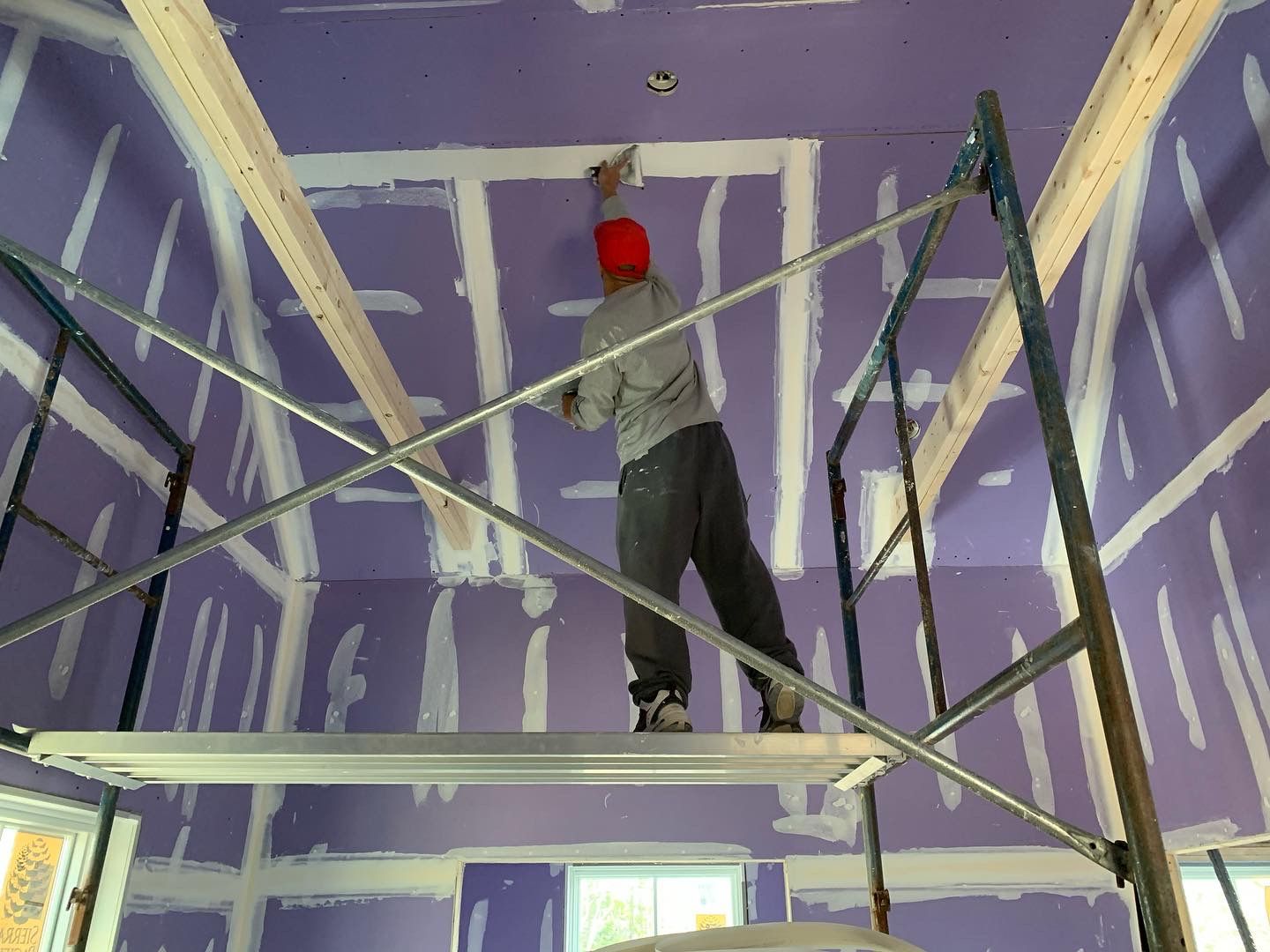 Worker on scaffolding painting or finishing a purple room ceiling with white trim lines.