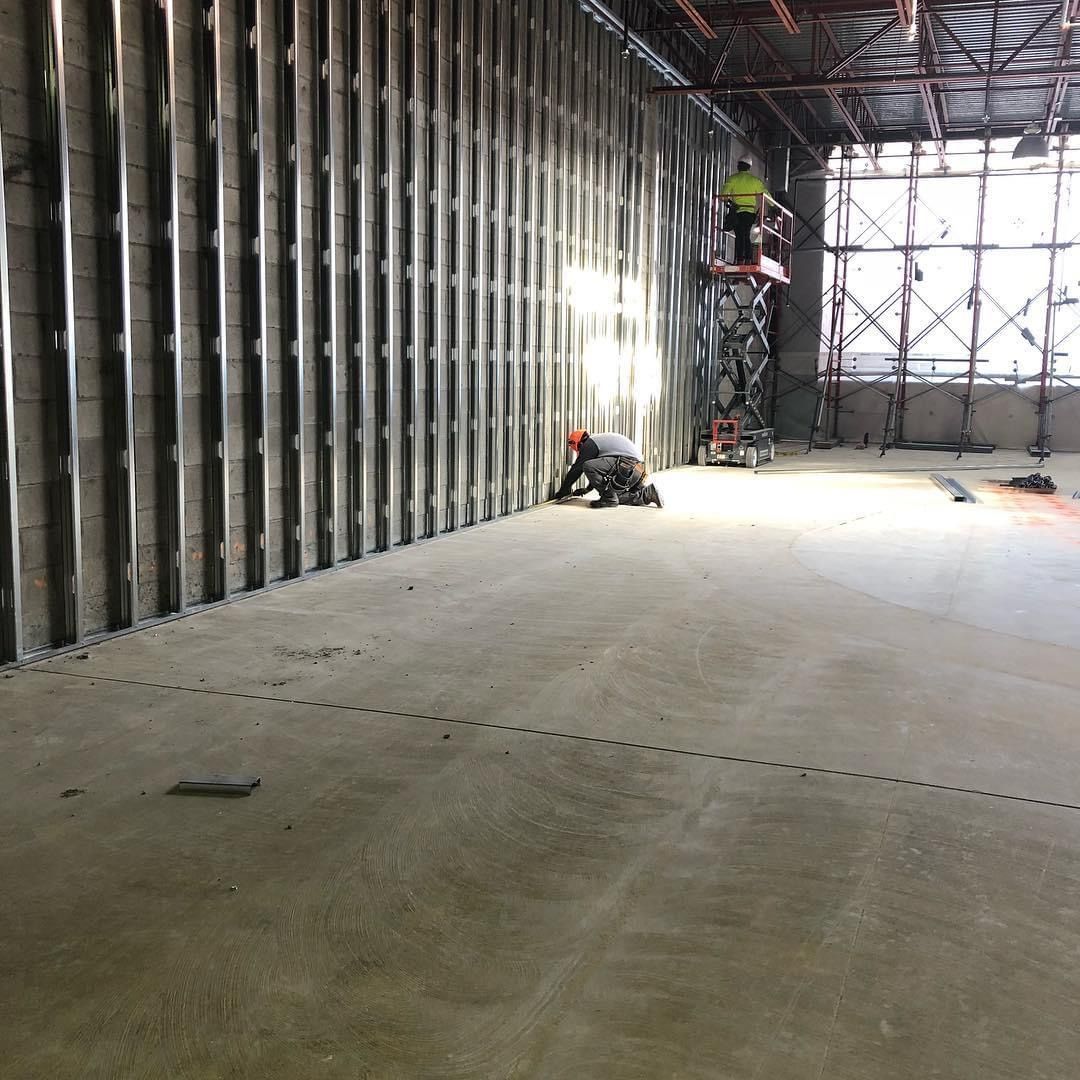 Construction site interior with metal framing, scaffolding, and workers on a concrete floor
