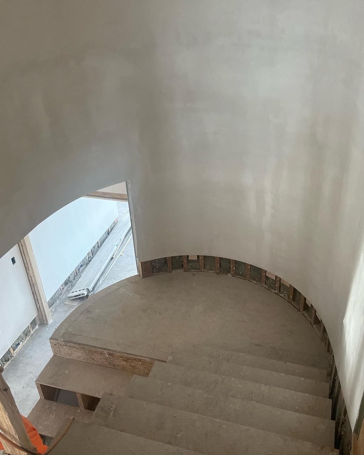 Curved indoor staircase with beige walls and unfinished steps, viewed from above.