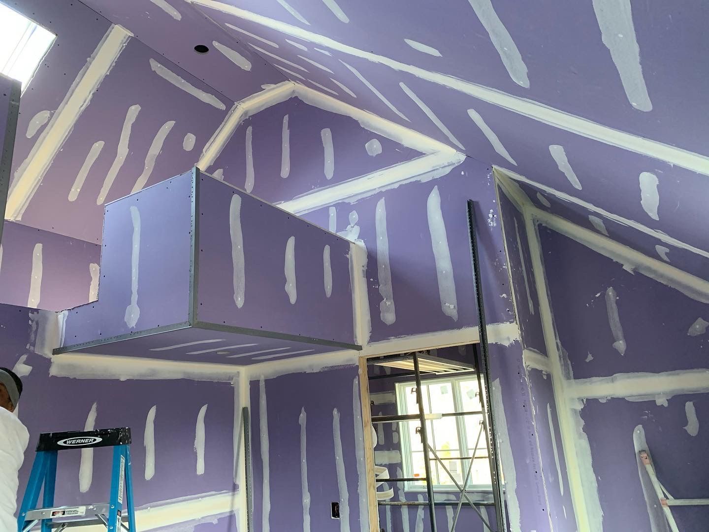 Partially finished room with purple drywall, white joint compound, window, and ladder against the wall