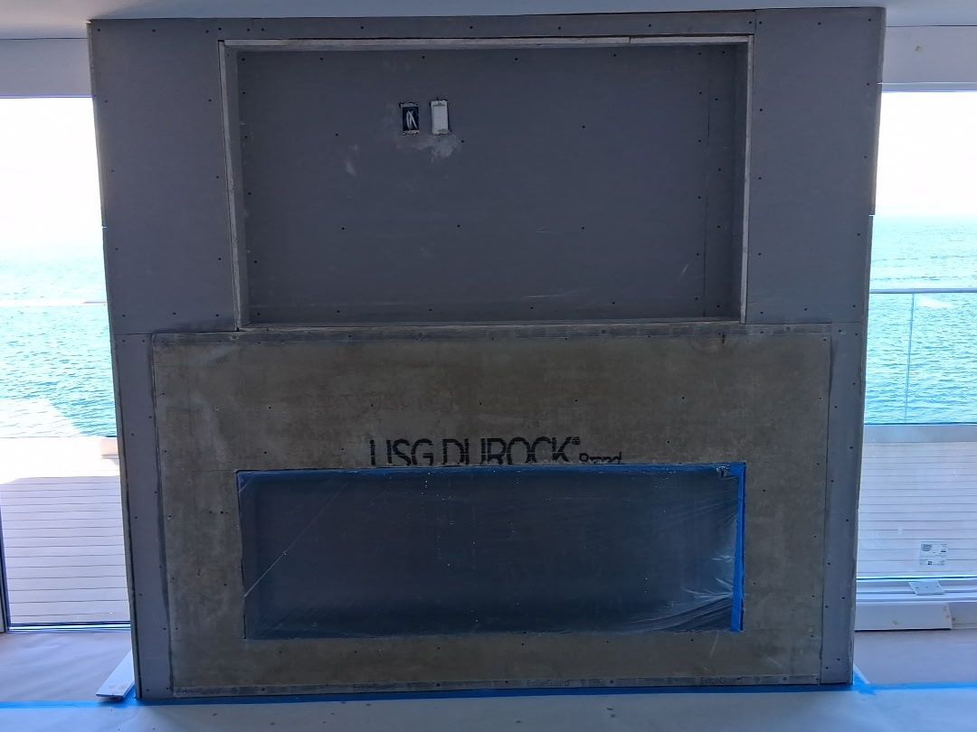 Gray rectangular structure on a boardwalk overlooking the ocean, with a small opening and blue-trimmed panel.