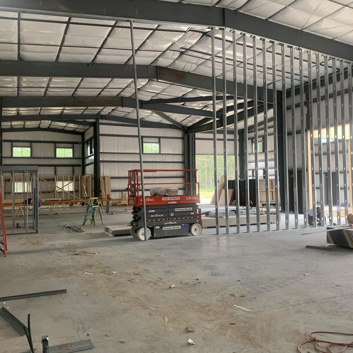 Interior of a steel-frame building under construction, with scaffolding and a scissor lift on a concrete floor.