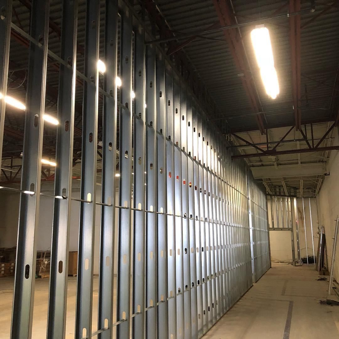 Interior construction site with metal stud framing and bright overhead lights in a long corridor