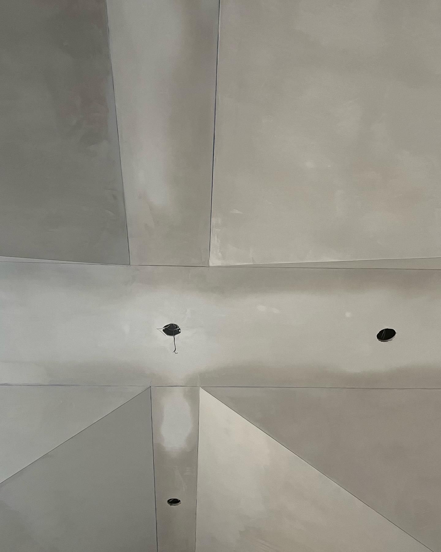Gray and white ceiling panels with recessed lights and seams forming geometric lines