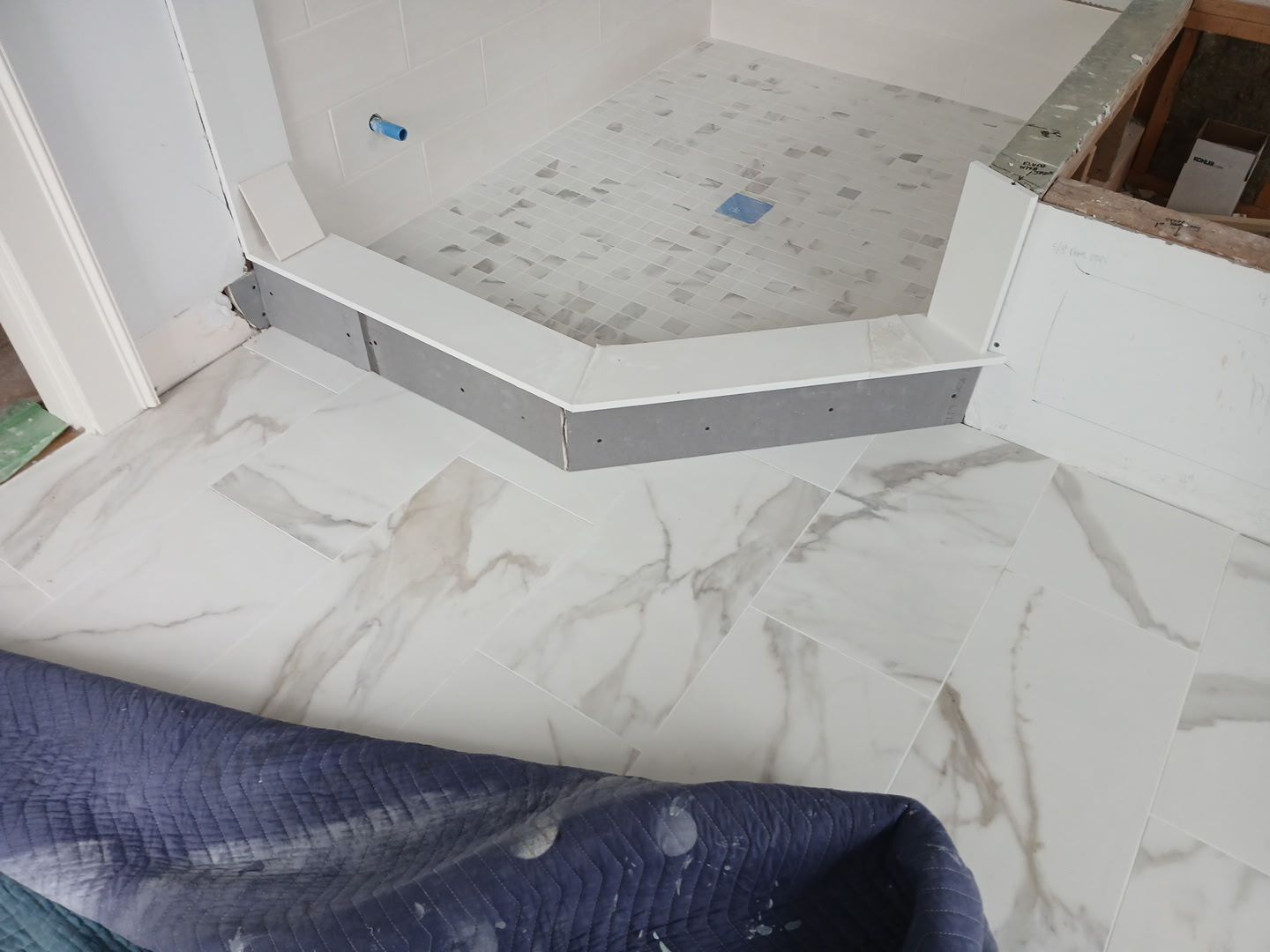 Marble-look floor with a raised step into a tiled area, partially covered by a rolled blue protective mat