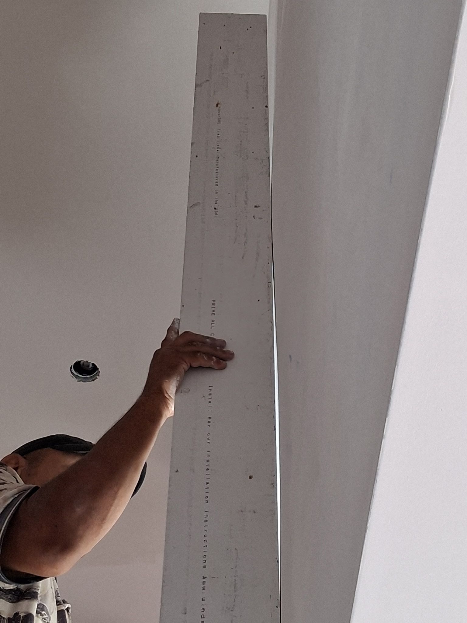 Person reaching up to measure a tall white column indoors