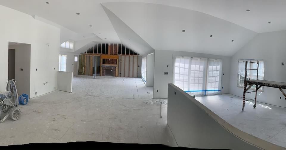 Large unfinished white interior with vaulted ceiling, exposed framing, and construction materials scattered around.