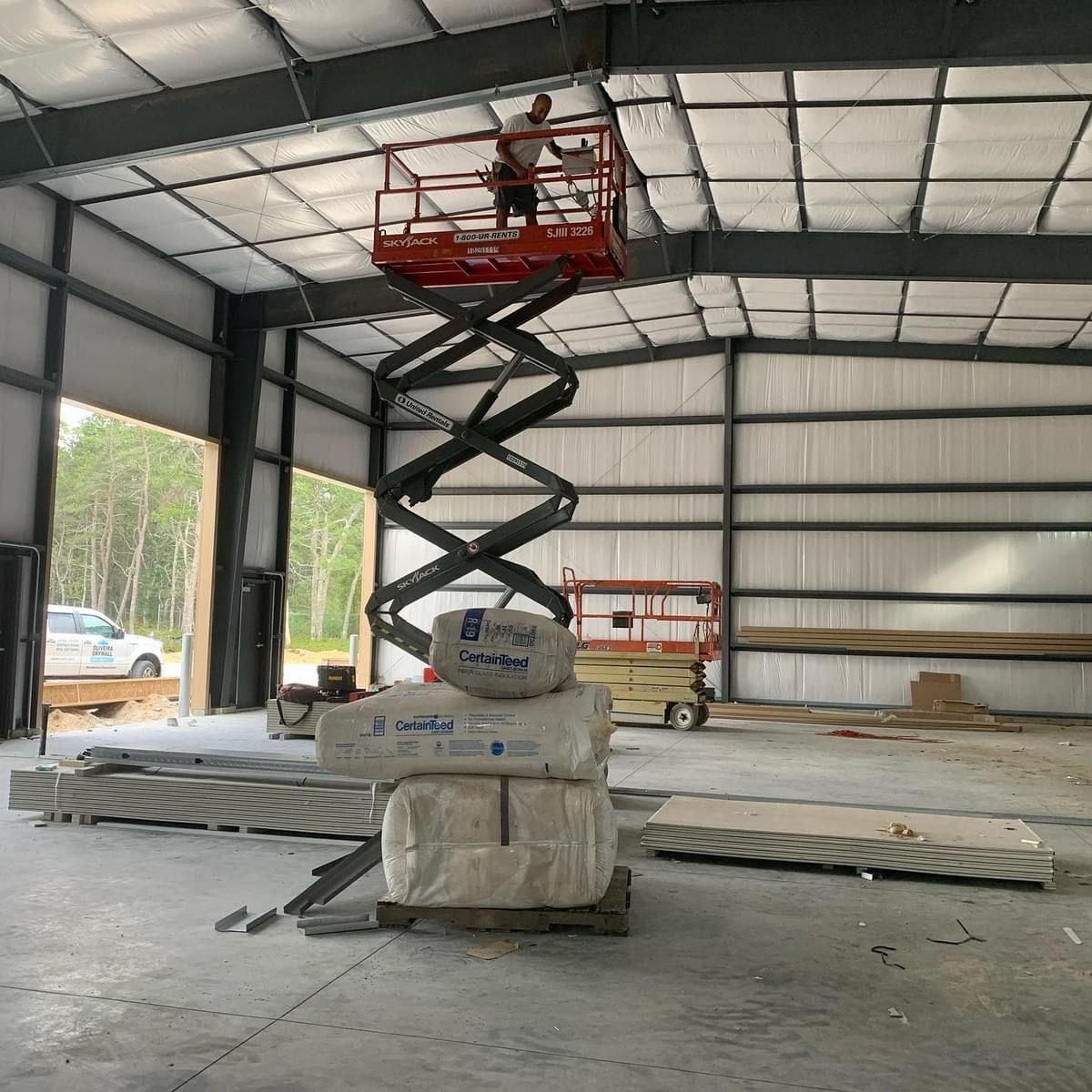 Scissor lift raising a worker inside a metal warehouse under construction.