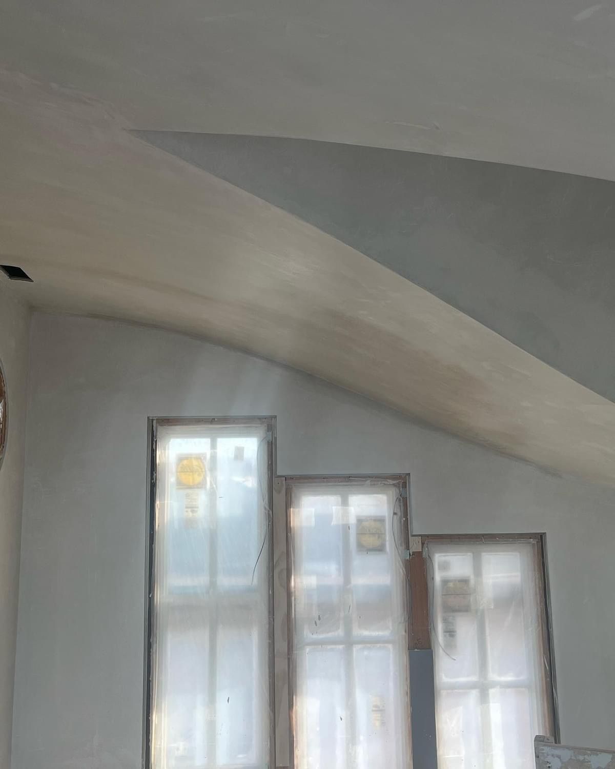 Sloped white ceiling above three tall windows with sheer curtains in a bright room
