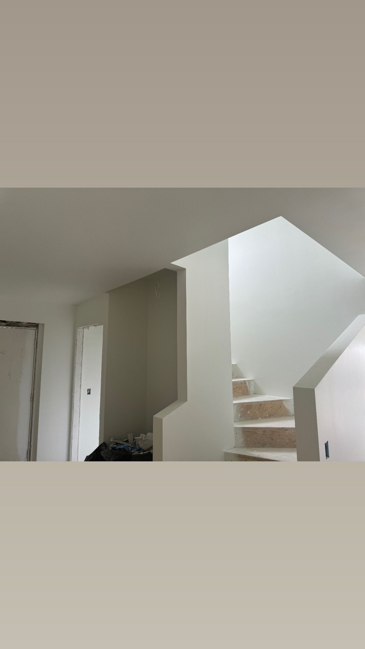 Interior of a house with a staircase, white walls, and a doorway leading to another room.